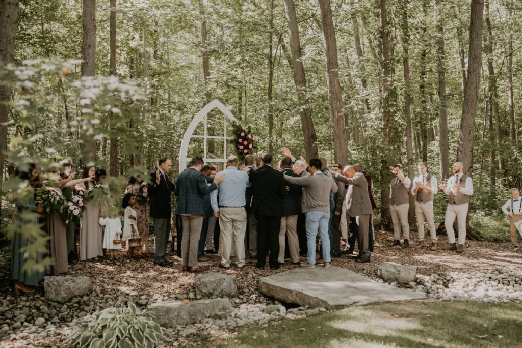 Wedding ceremony image at The Clearing in Shedden, ON. All of the men who attend the ceremony are encircling the bride and groom in prayer.