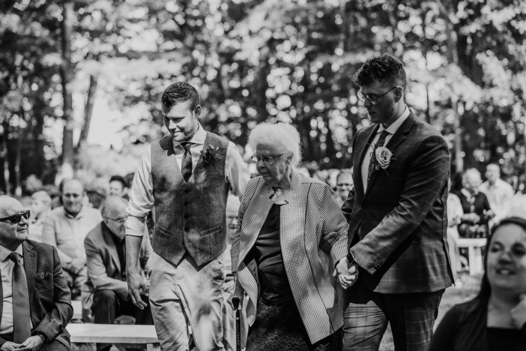 Black and white image of a groom and his brother escorting is grandmother down the aisle at The Clearing in Shedden, ON.