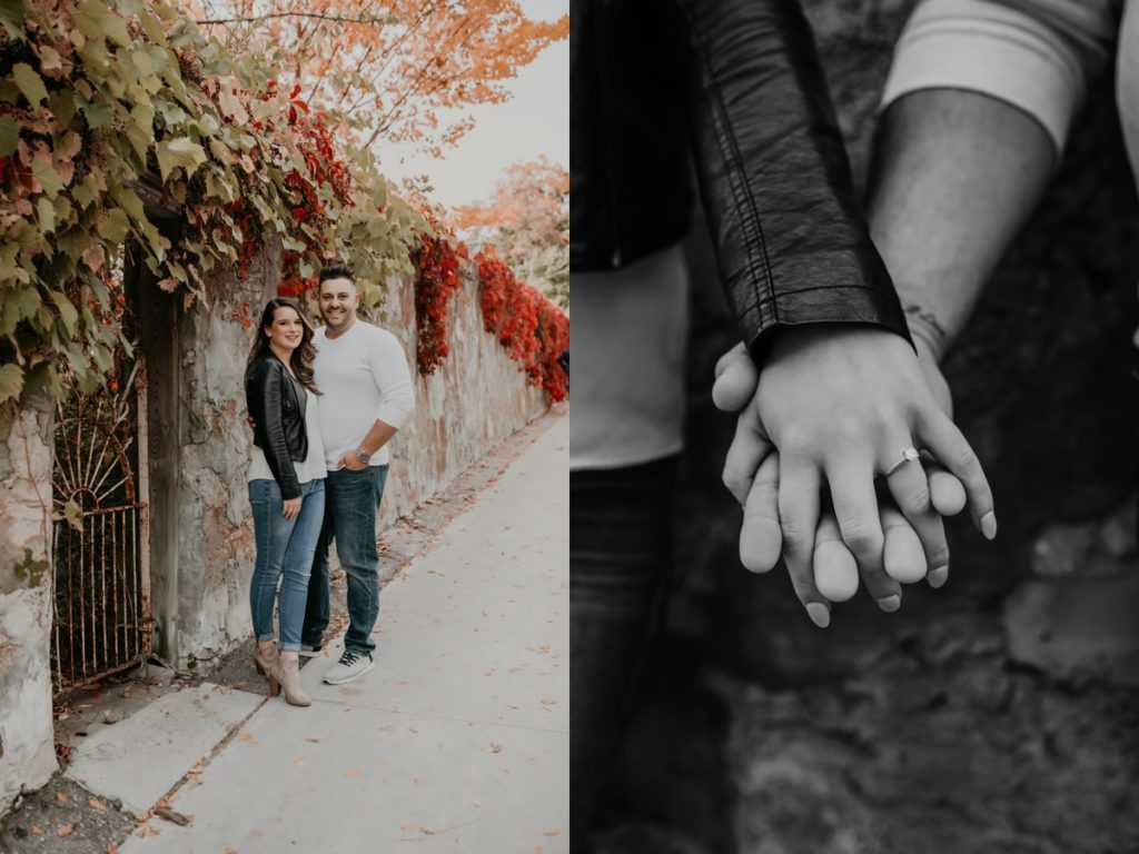 Couple pose for engagement photos beside a rustic stone wall. Some of the greenery draping overtop of it has turned bright red with the seasonal change. The man and woman are cuddling and smiling at the camera. Captured by best london ontario wedding and engagement photographer ashlee ellison.