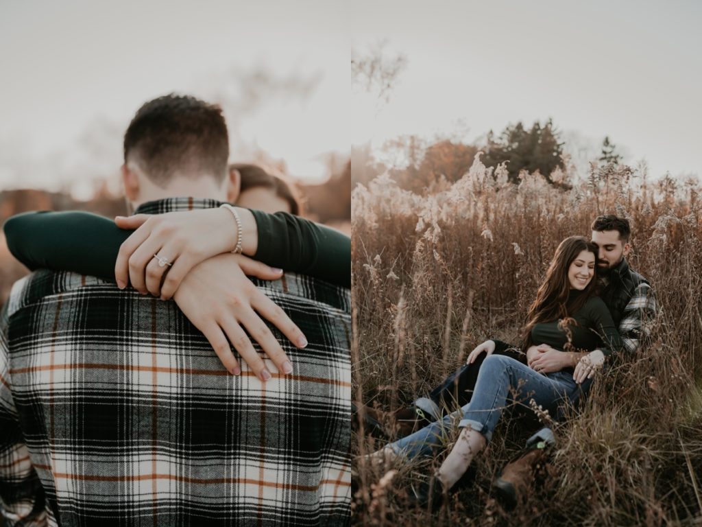 Couple sit in long grasses for an intimate london ontario engagemenet photo. They are cuddling and smiling with their eyes closed.