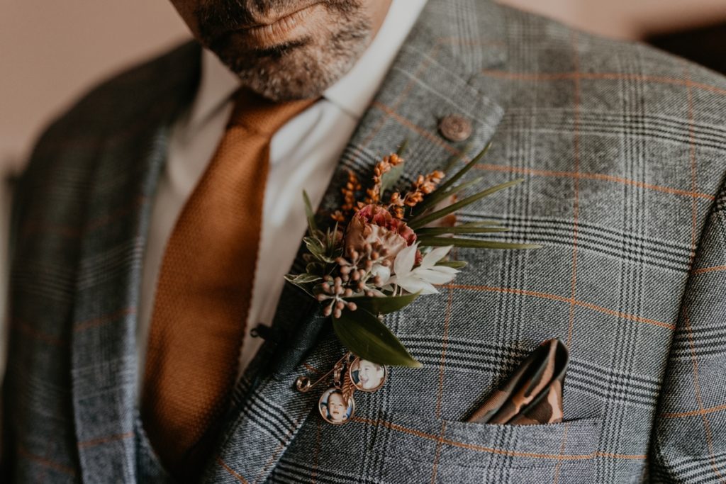 Close up image of groom's boutonniere that feature two small memory photos of departed loved ones. Groom is looking down at the boutonniere and the image is cropped so you can only see his lips. Captured by best London, Ontario wedding photographer Ashlee Ellison.