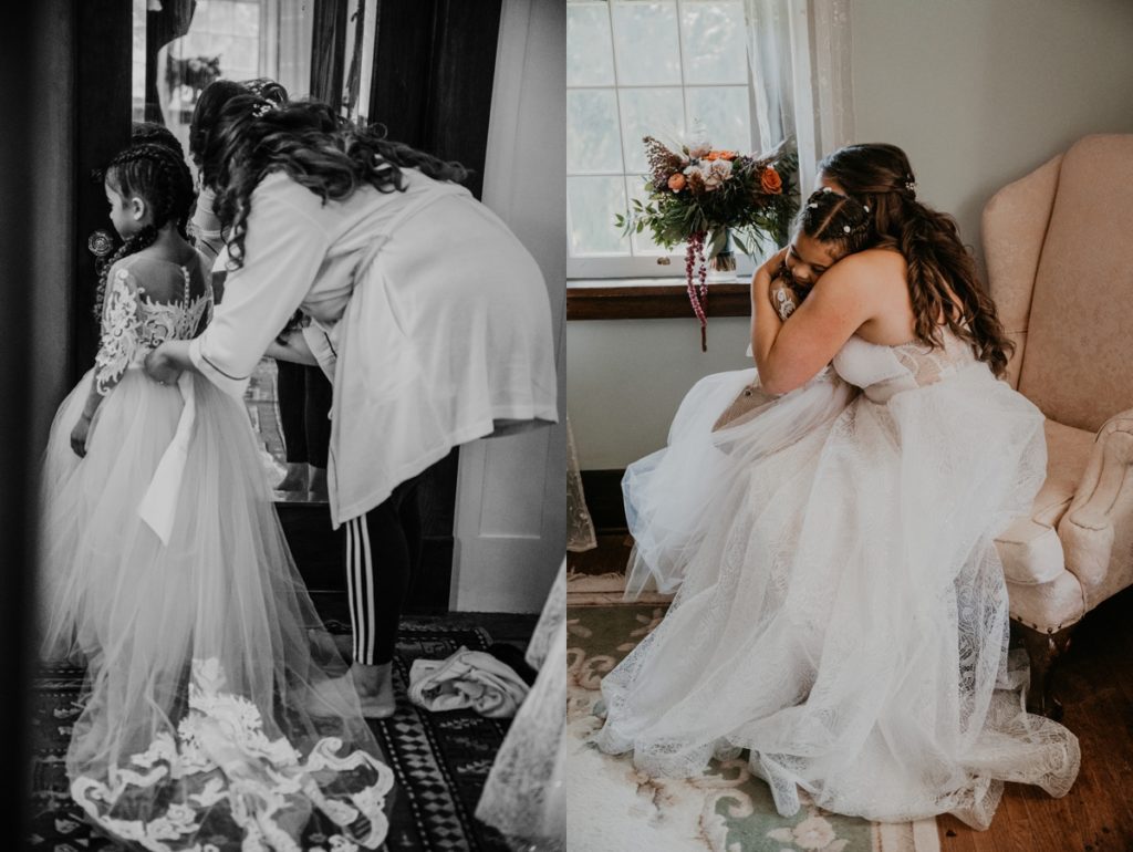 A bride and her daughter, who is also her flower girl, share a tender hug as they sit on a blush velvet arm chair after they are ready for the wedding. The brides bouquet rests on the window sill behind them.