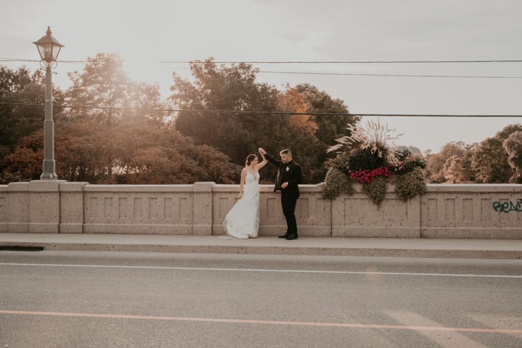 Bride and groom share a private slow dance at golden hour on a bridge in St Jacobs Ontario. The groom is twirling is bride as the sun sets behind them.