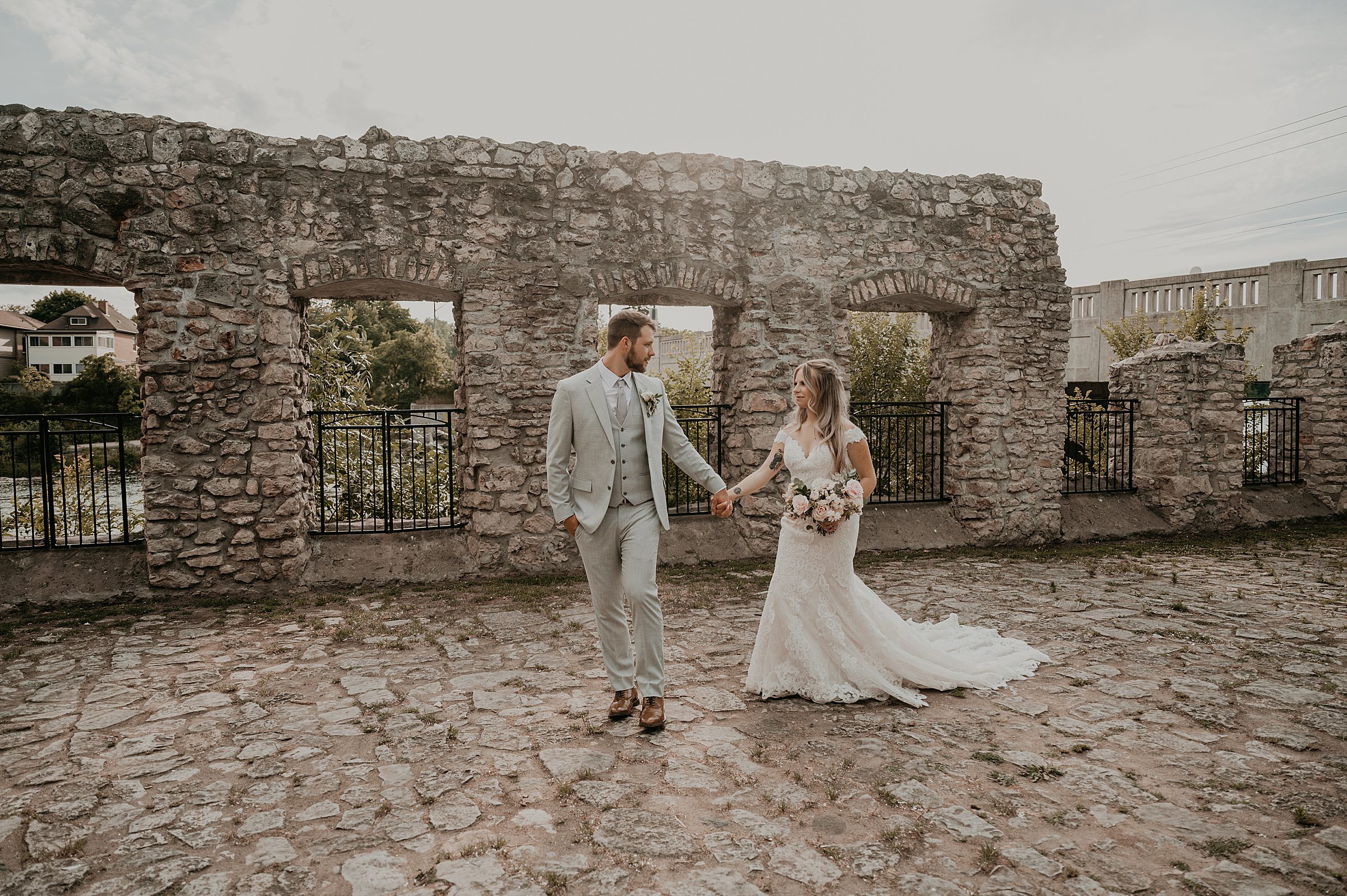 Bride and groom walk amongst the mill race park ruins for a candid wedding day photo.