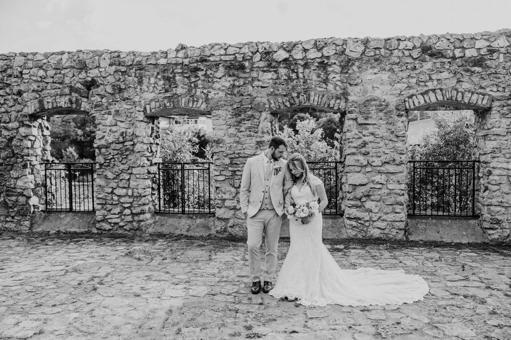 Bride and groom are walking against the stone ruins at Mill Race Park on their wedding day.