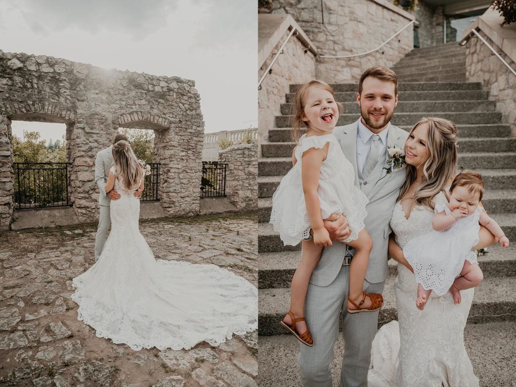 Bride and groom stand at the steps of the Cambridge Mill with the groom holding their toddler and the bride holding their infant. The groom is smiling at the camera and the bride is smiling at her toddler.