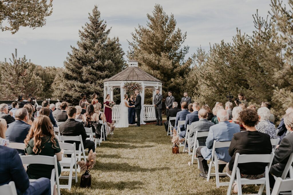 Guests watch as a bride and groom exchange vows at the century barn in denfield ontairo. captured by top london ontario wedding photographer ashlee ellison.