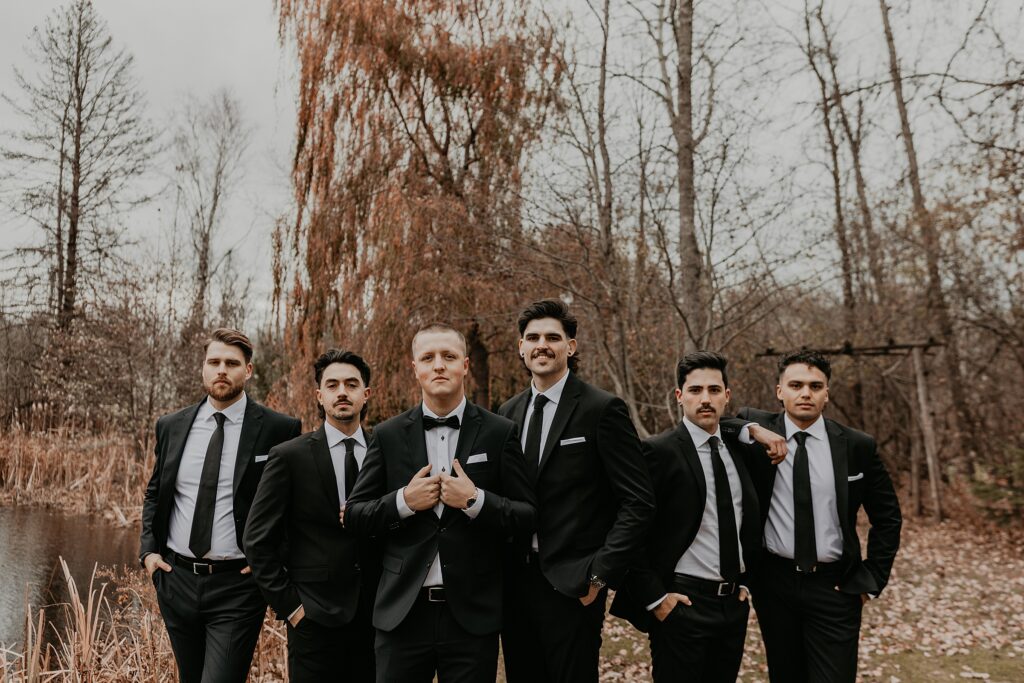 Groom and his groomsmen pose for a GQ-esque wedding photo. Groom is holding his label, groomsmen are standing casually with hands in pockets with a straight face.