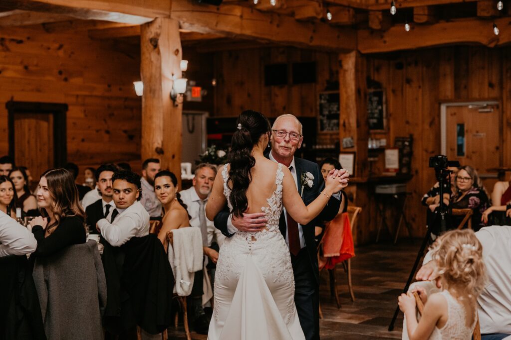 Bride and her father share a first dance at her holland marsh wineries wedding. Image of bride's back and dad is looking over bride's shoulder looking at the camera.
