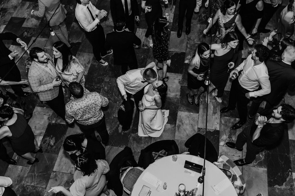 Black and white image of bride and groom sharing a kiss on the dance floor at their Holland Marsh Wineries wedding as their guests are dancing around them. Captured by best newmarket wedding photographer ashlee ellison.