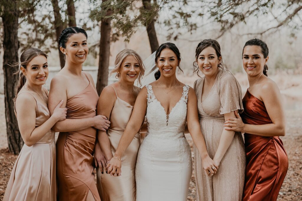 Bride and her bridesmaids hold hands and link arms as they pose for a girls portrait at her holland marsh wineries wedding in newmarket, ON. captured by best newmarket wedding photographer ashlee ellison.