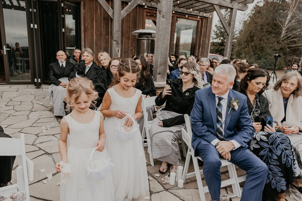 Two flower girls are throwing petals as they walk down the aisle at a holland marsh wineries wedding ceremony in newmarket, ontario.