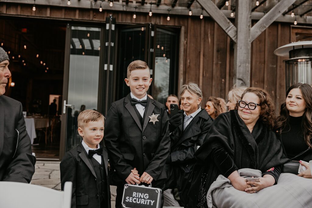 Two ring bearers are walking hand-in-hand down the aisle at a holland marsh wineries wedding ceremony in newmarket ontario.
