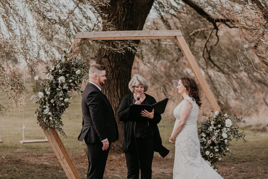 Couple exchange vows during their Crescent Hill Acres wedding ceremony. Bride and groom are looking at each other. Captured by top Ontario wedding photographer Ashlee Ellison.
