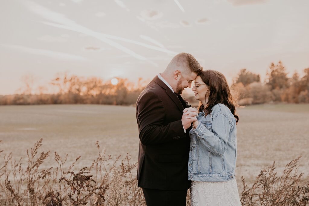 Intimate golden hour portrait of bride and groom in a field at crescent hill acres. bride and groom are facing each other, touching foreheads and holding hands. captured by top sarnia wedding photographer ashlee ellison.