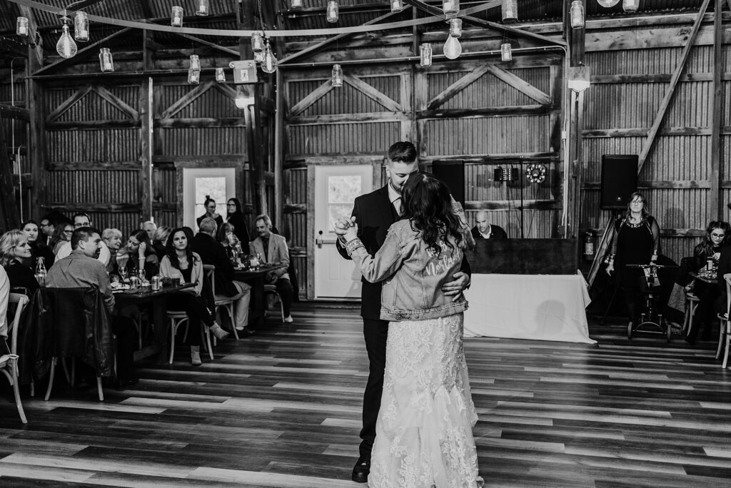 Black and white image of bride and groom sharing their first dance in the barn at crescent hill acres in plympton-wyoming. captured by sarnia wedding photographer ashlee ellison.