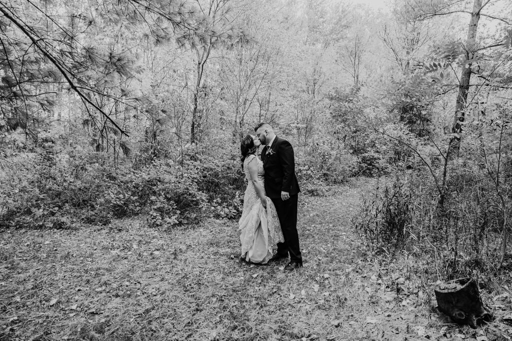 Black and white image of bride and groom sharing a kiss in a wooded area at crescent hill acres wedding venue. captured by top sarnia wedding photographer ashlee ellison.