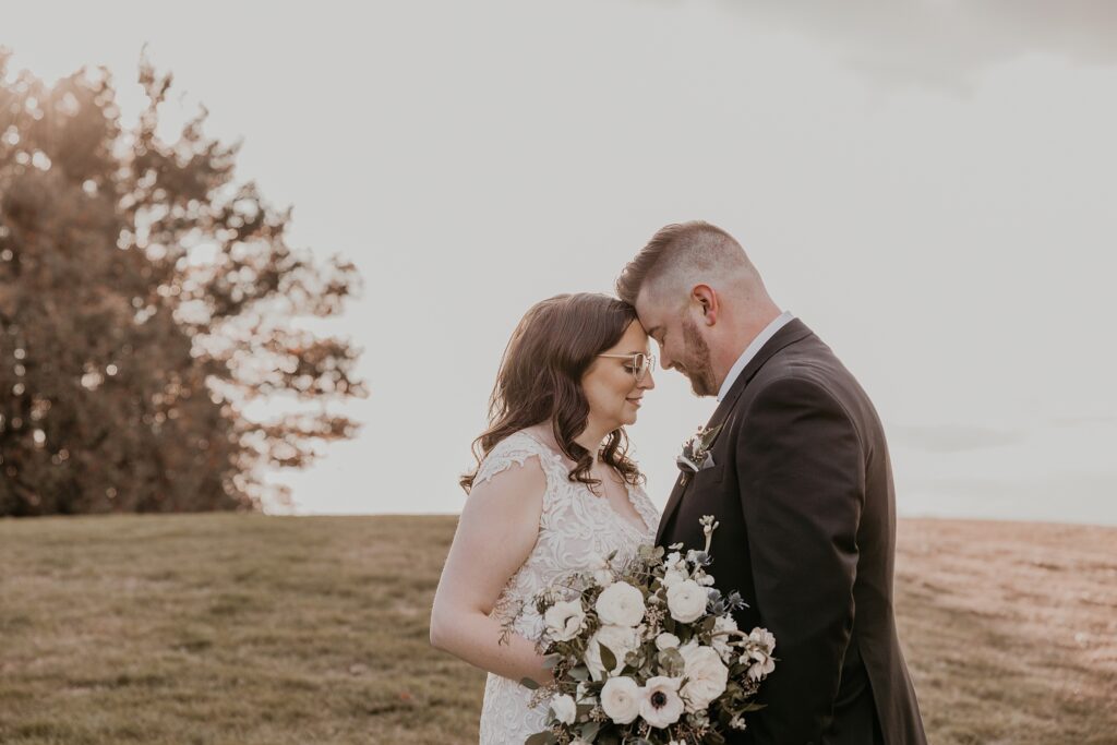 Bride and groom stand for an intimate wedding portrait at crescent hill acres. their heads are touching in a field with the brides anemone bouquet in front of them. captured by sarnia wedding photographer ashlee ellison.